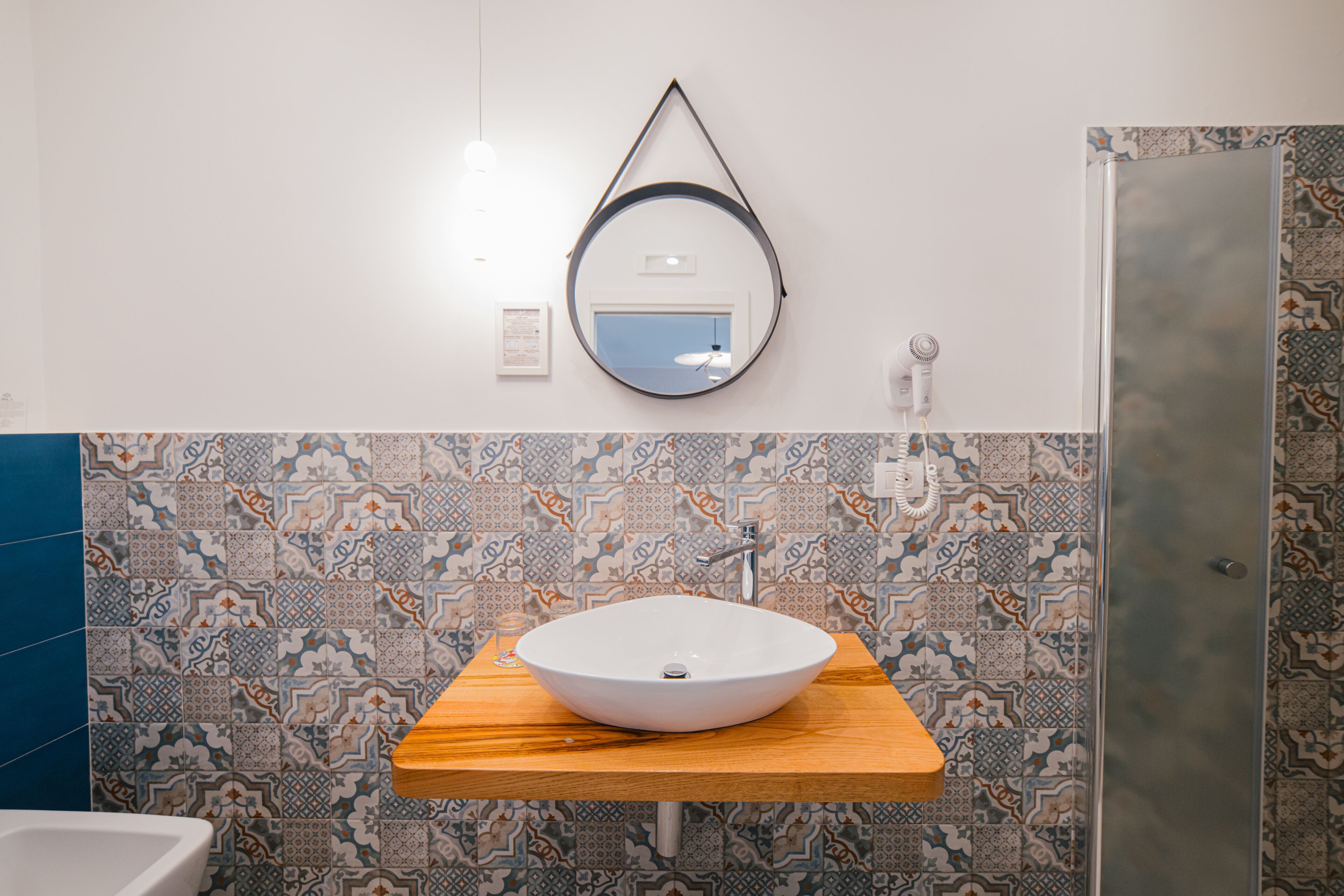 A bathroom with a wooden vanity, a round mirror, and patterned tiles.