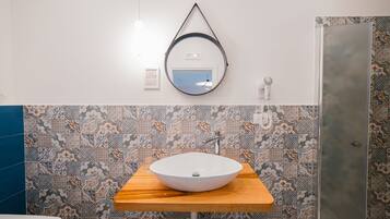 A bathroom with a wooden vanity, a round mirror, and patterned tiles.
