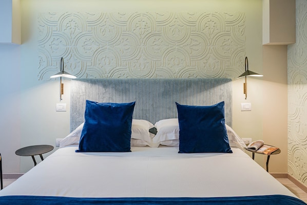 A hotel room with a large bed, two blue pillows, a textured wall, and two wall-mounted lamps.