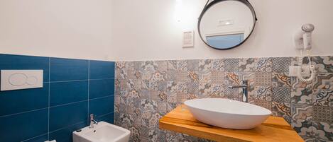 Een badkamer met een wit wastafel op een houten aanrecht, een bidet en een spiegel bevestigd aan de muur.