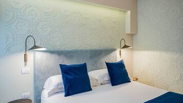 Habitación de hotel con cama, dos almohadas azules, una mesita de noche y una pared con diseño decorativo.