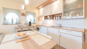 Une cuisine moderne avec des meubles blancs, un plan de travail en bois et une fenêtre équipée de stores.