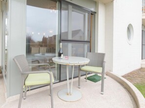 Eine Terrasse mit zwei Korbstühlen und einem kleinen runden Tisch, einer Weinflasche und einem Glas.
