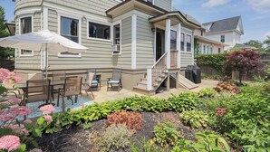 A two-story house with a covered patio area, outdoor seating, and a garden with various plants and flowers.