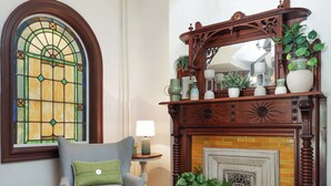 A room with a fireplace, a chair with a cushion, a rug, and a stained glass window.