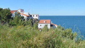En fastighet vid kusten med vita byggnader och röda tak, omgiven av grönska och med utsikt över havet.