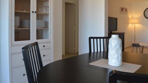 En matplats med ett mörkt, runt bord, två svarta stolar, en vit vas, ett skåp med glasdörrar och en klocka på väggen.