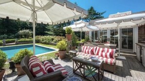 Ein Poolbereich mit Gartenmöbeln, Sonnenschirmen und Blumentöpfen.