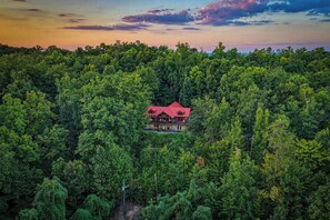 A lodge surrounded by dense forest, with a prominent red roof and multiple windows. - Epic Mountain Views + Hot Tub + Theater + Games | Private 5 BR Getaway (Pigeon Forge)