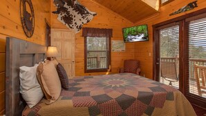 A cozy room with a bed, a television, and a large window with blinds. - Epic Mountain Views + Hot Tub + Theater + Games | Private 5 BR Getaway (Pigeon Forge)