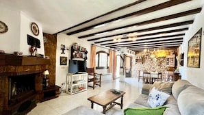A cozy living room with a fireplace, a television, and a dining area with a stone wall.