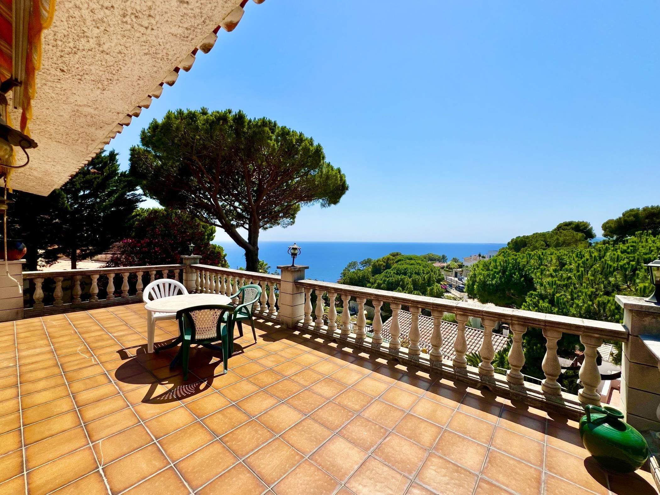 Um terraço com mesa e cadeiras, um corrimão e vista para o mar.