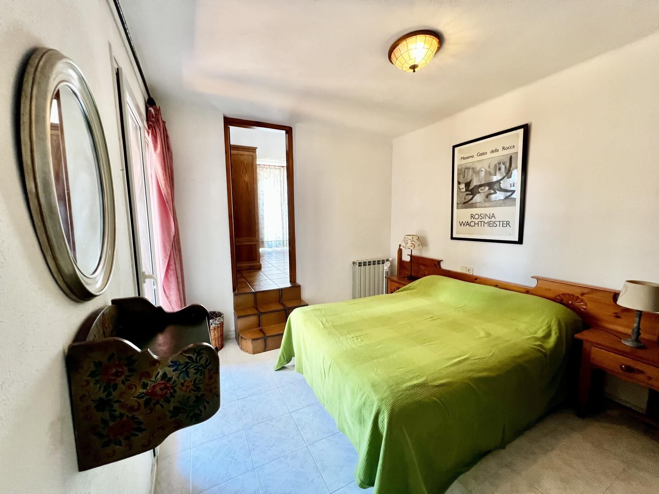 A bedroom with a bed, a chair, a radiator, a mirror, and a framed picture on the wall.