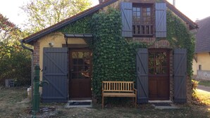 Une maison rustique aux murs couverts de lierre, avec un banc en bois et un potelet d’hydrant vert.