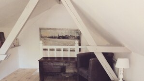 Une chambre mansardée chaleureuse, avec un plafond en pente, un lit en bois, une petite chaise, une lampe et une tête de lit rustique.