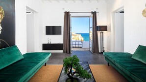 A modern living room with a green sofa, a coffee table with a bonsai tree, and a view of the sea through a glass door. - Casa Magnolia - Luxury villa with private heated pool and sea views! (Carvoeiro)