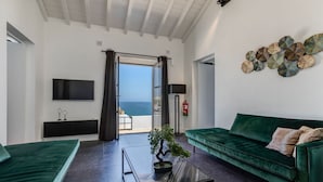 A modern living room with a green sofa, a coffee table, and a TV. There is a view of the sea through a large window. - Casa Magnolia - Luxury villa with private heated pool and sea views! (Carvoeiro)