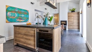 A modern kitchen with a wooden island, built-in oven, and a large decorative fish painting. - Casa Magnolia - Luxury villa with private heated pool and sea views! (Carvoeiro)