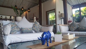 Una sala de estar moderna con un sofá blanco, cojines estampados, una escultura de toro azul y una mesa de centro de vidrio.