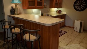 A kitchen with a central island, bar stools, wooden cabinets, a clock, and a refrigerator.