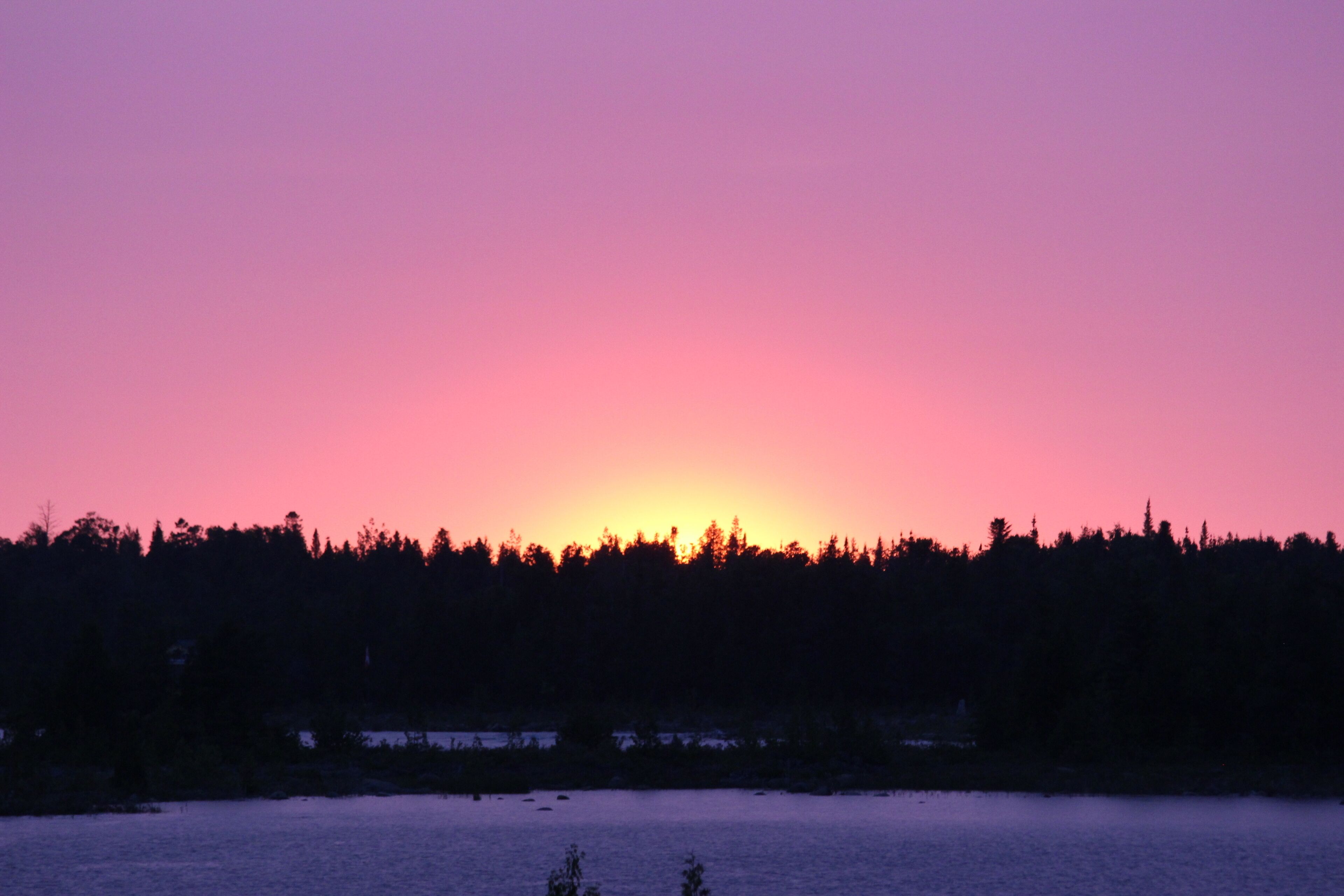 A sunset over a forested area with a body of water in the foreground.