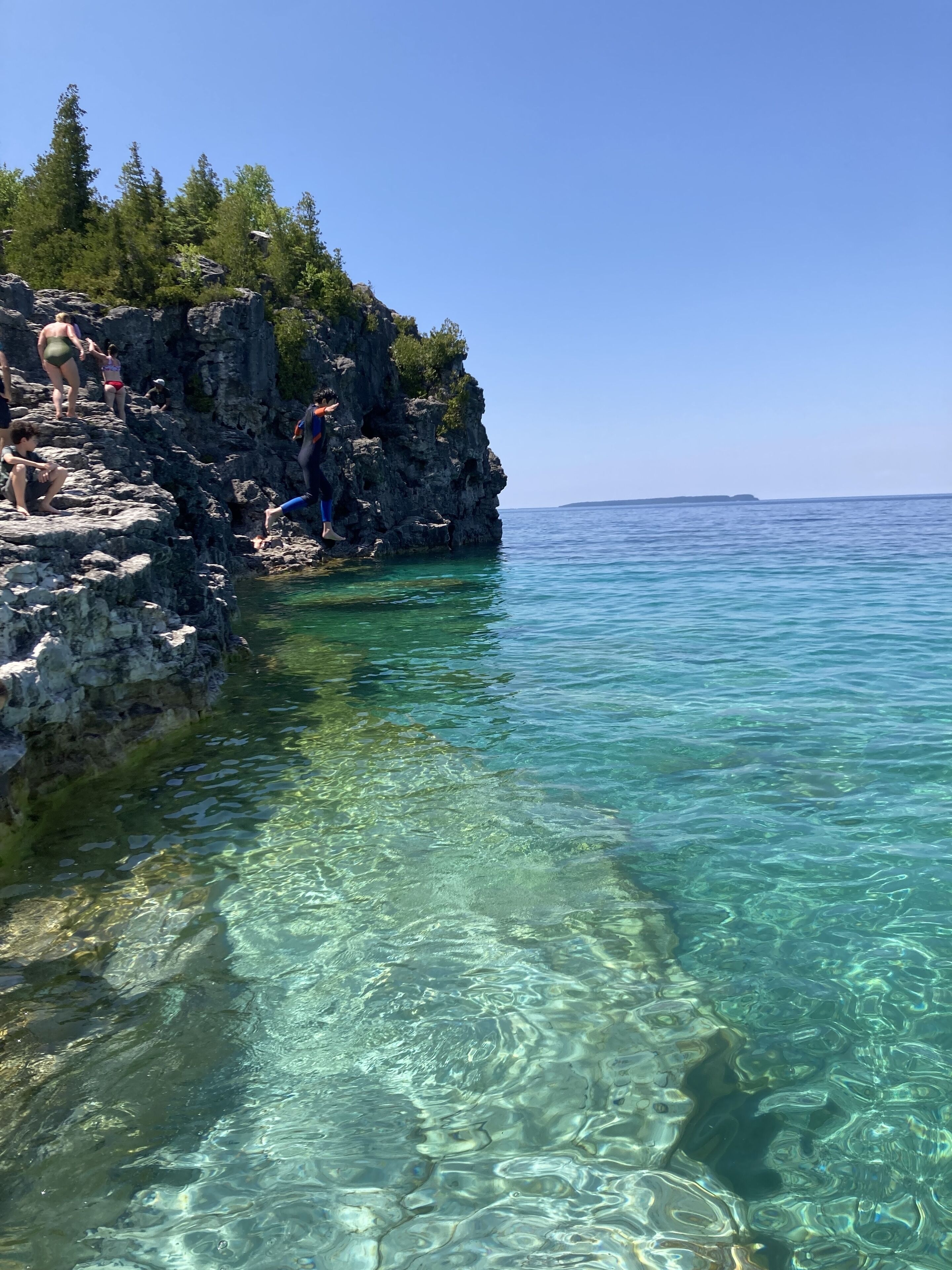 A rocky coastline with clear water and a distant island.