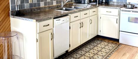 A kitchen with white cabinets, a granite countertop, a dishwasher, a coffee maker, and a patterned rug.