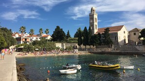 Un pueblo costero con una torre destacada, una playa con gente y barcos en el agua.