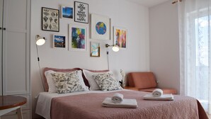 Un dormitorio ordenado con cama, almohadas, una silla y decoración en la pared.