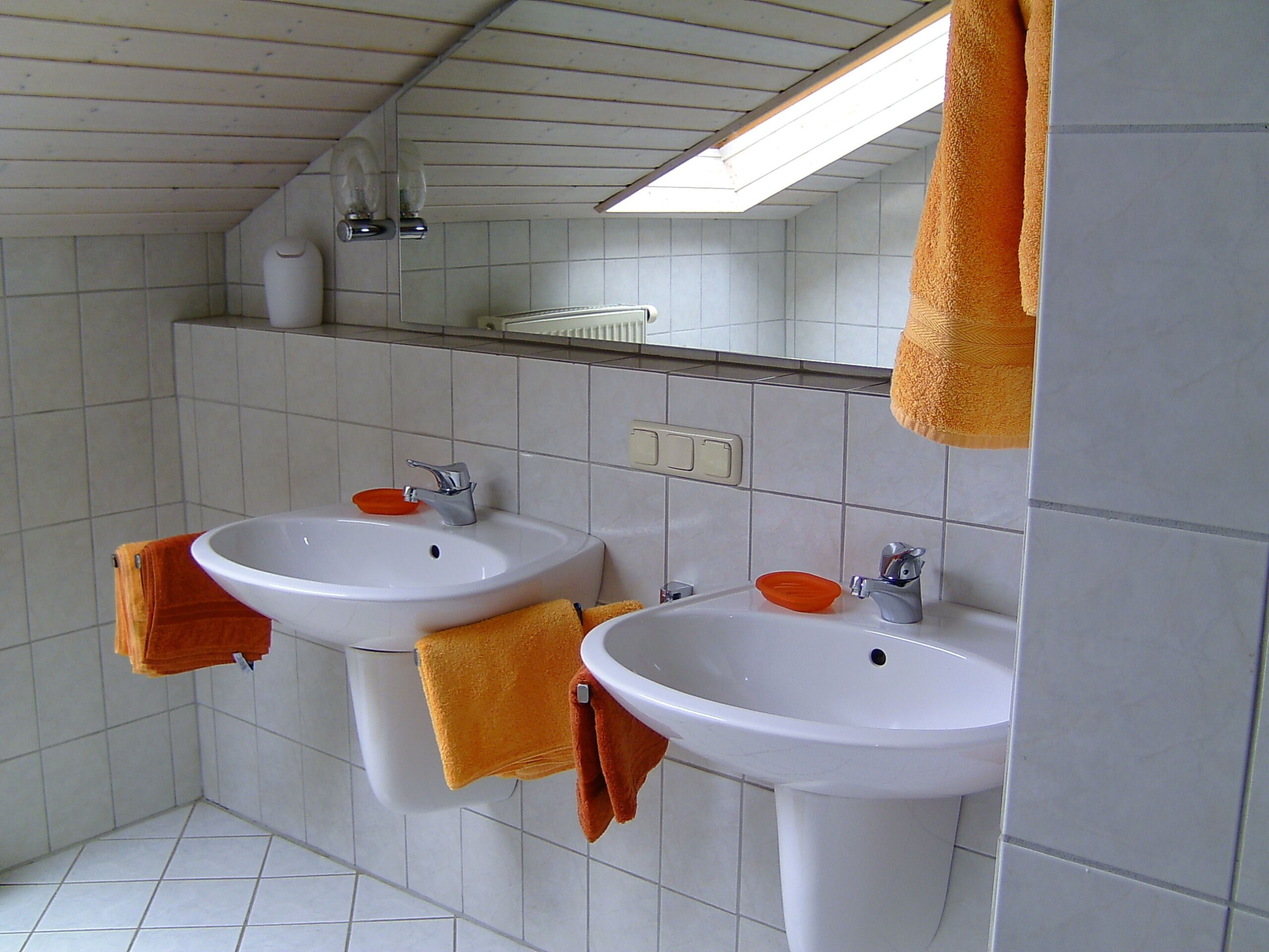 A bathroom with two sinks, a mirror, and a skylight.