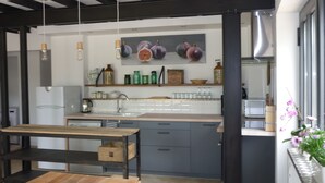 A modern kitchen with a wooden table and bench, a sink, and decorative items on shelves. - Workshop n°2 for 6 with shared pool and sauna for lazy days (Semur-en-Auxois)