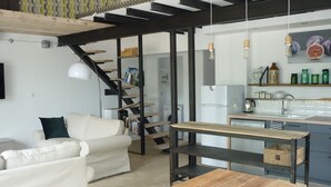 A modern kitchen with a wooden table, a white sofa, and a staircase leading to another level. - Workshop n°2 for 6 with shared pool and sauna for lazy days (Semur-en-Auxois)