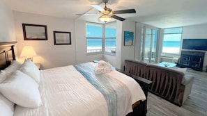 A hotel room with a bed, a desk, a television, and a view of the ocean.