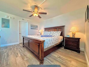 A bedroom with a wooden bed, a ceiling fan, a nightstand, and a lamp.