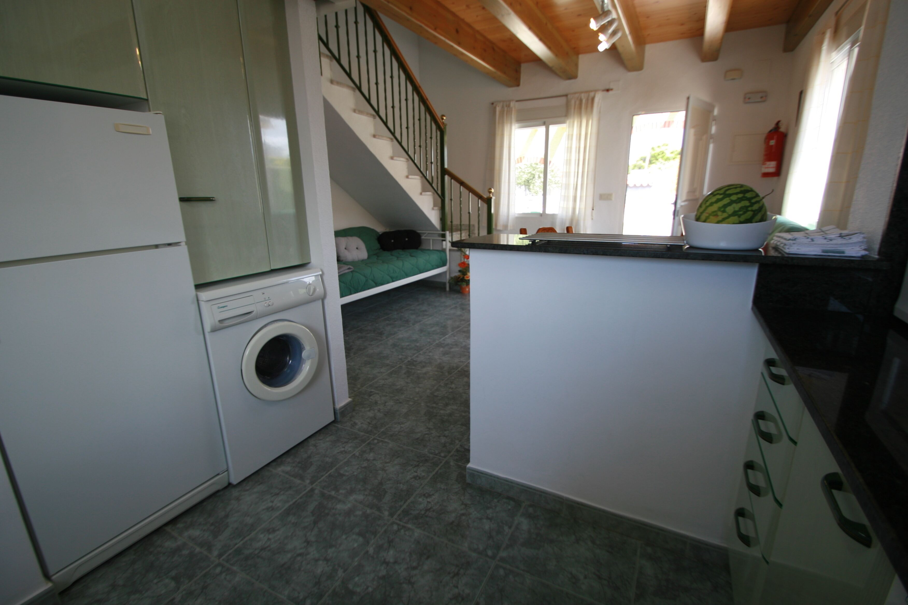 Cocina compacta con lavadora, un pequeño comedor y una escalera que sube a una cama en un altillo.