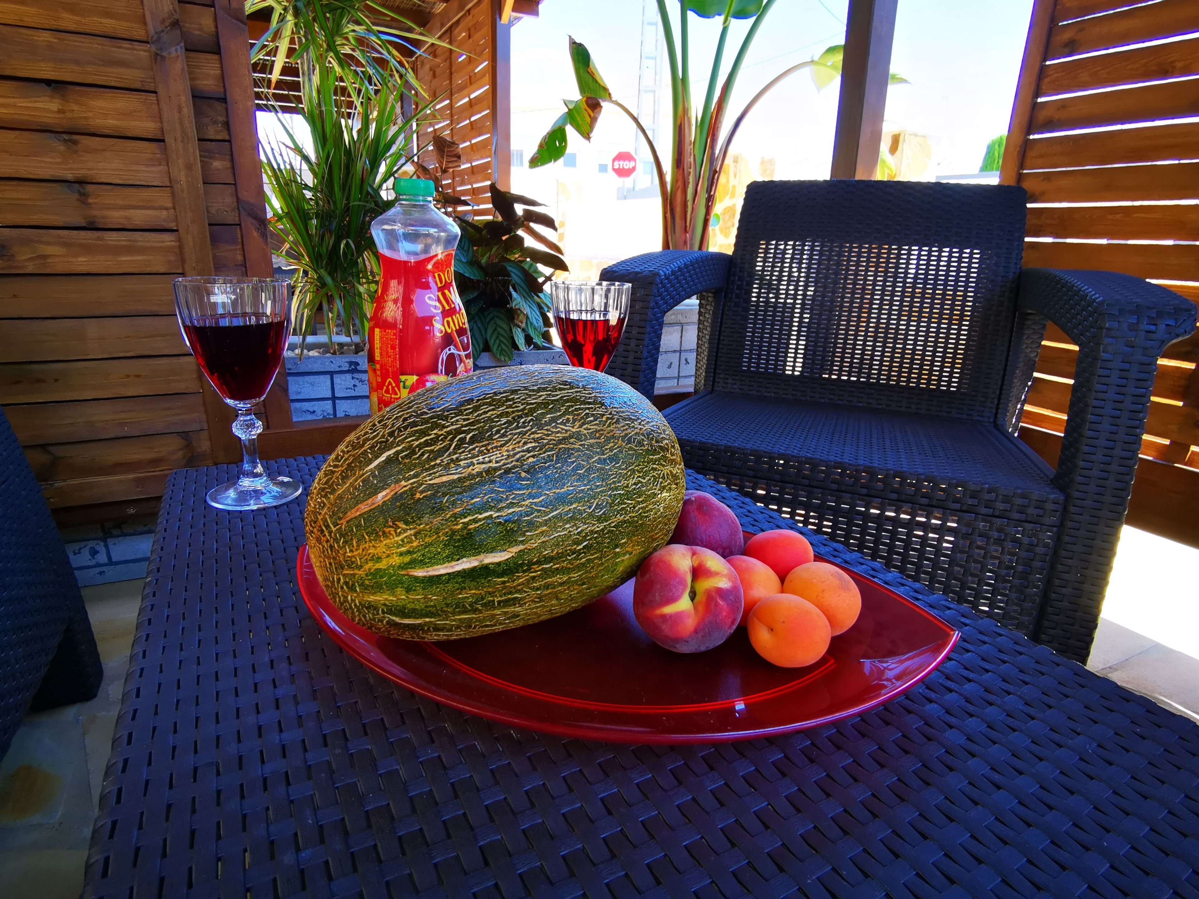 A table with a red plate of fruits, a glass of red wine, and a bottle of soda.
