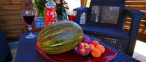 A table with a red plate of fruits, a glass of red wine, and a bottle of soda.