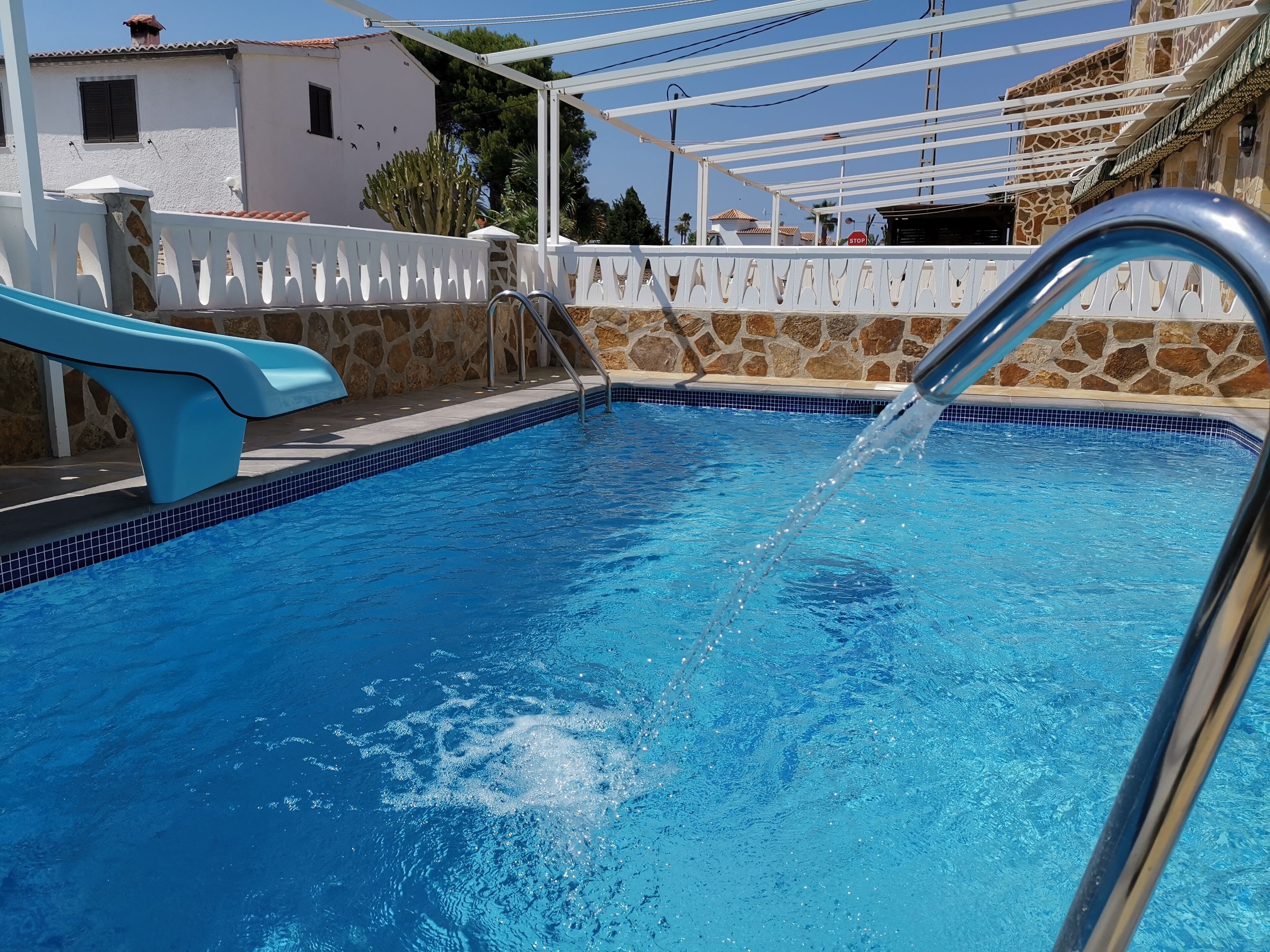 A swimming pool with clear blue water, a metal ladder, and a white pergola structure.