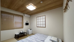 A room with a wooden ceiling, a bed with patterned bedding, a small table with a kettle, and a wall-mounted air conditioner. - Karin Doo Hotel (Tomisato)