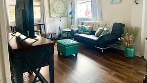 Un salon avec un canapé, un pouf et un téléviseur posé sur un meuble.