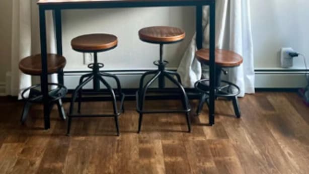 Un coin repas avec une table et quatre tabourets, une fenêtre avec des rideaux et un tableau accroché au mur.