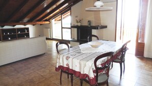 A dining area with a table set for four, wooden chairs, a white tablecloth, and a hanging pendant light. - Attic overlooking the sea of the Cyclops (Vampolieri)