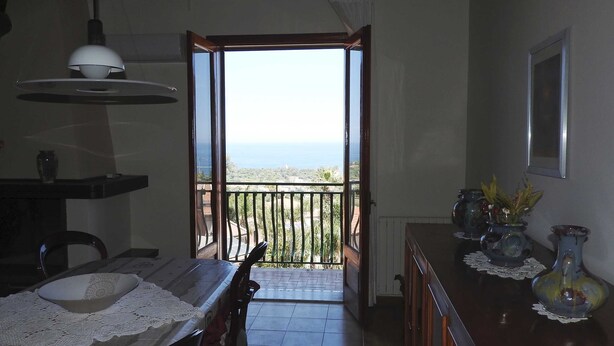 A room with a balcony, a dining table with a bowl, and a vase with flowers. - Attic overlooking the sea of the Cyclops (Vampolieri)