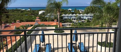 A balcony with blue lounge chairs and a view of a resort with red-roofed buildings and a beach.