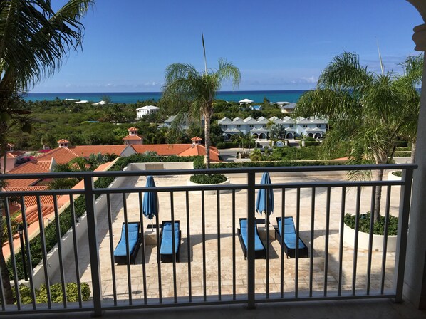 A balcony with blue lounge chairs and a view of a resort with red-roofed buildings and a beach.