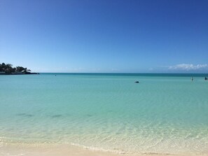 A beach with clear turquoise water, a sandy shore, and a distant shoreline with vegetation.