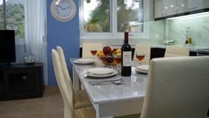 A dining area with a table set for two, a bowl of fruit, a bottle of wine, and a clock on the wall.