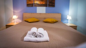 A neatly made bed with two rolled towels, two yellow pillows, and a wooden headboard.