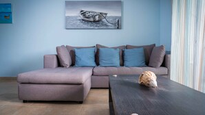 A modern living room with a grey sectional sofa, a dark wooden coffee table, and a large framed artwork of a boat on water.