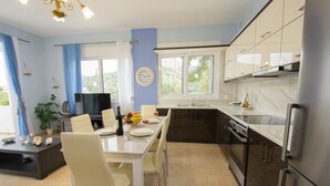 A modern kitchen with a dining area, featuring a TV, dining table, chairs, and a sink.